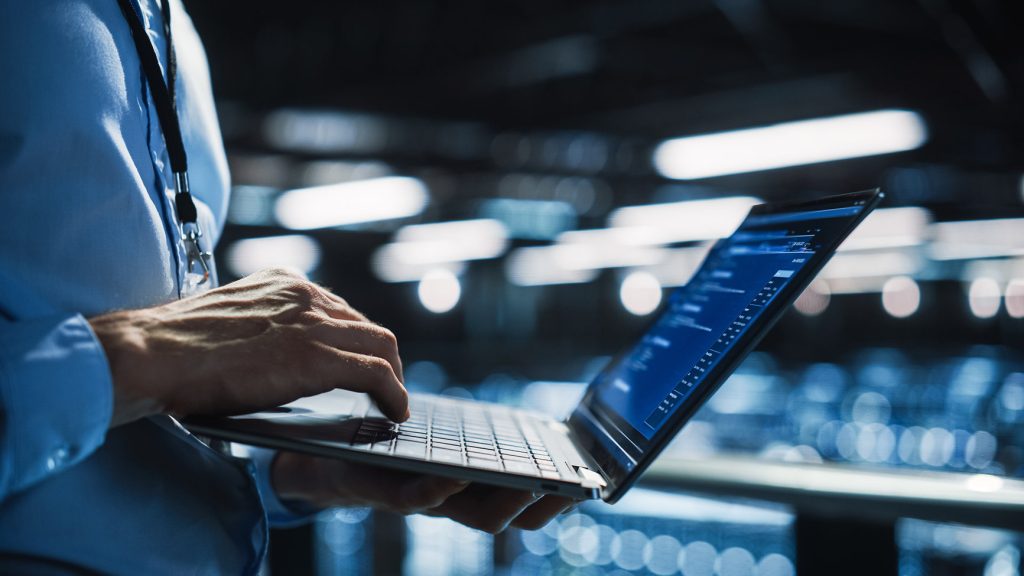 A person in a blue shirt types on a laptop, illuminated by soft, modern lighting in a tech environment.