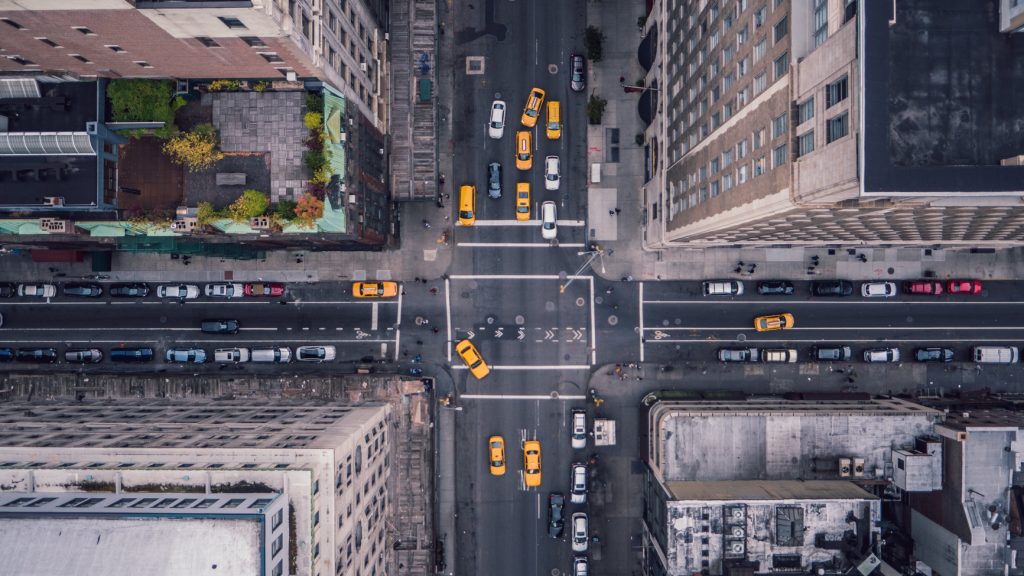 An aerial view of a busy city intersection filled with yellow taxis and various vehicles, surrounded by tall buildings.