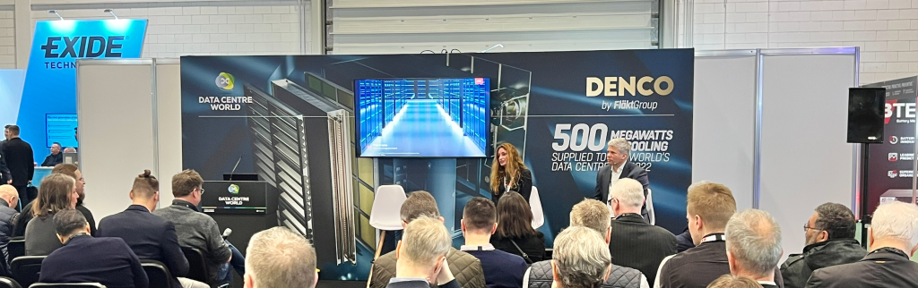 A conference presentation with a speaker, audience, and a large screen displaying data center information.