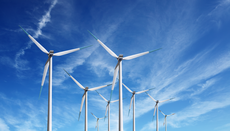 A series of wind turbines against a clear blue sky with wispy clouds.