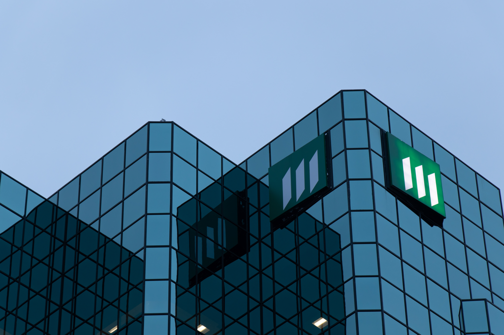 A modern glass building with a green logo prominently displayed on its facade against a twilight sky.