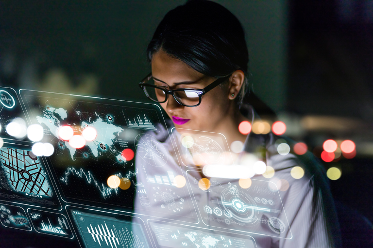 A woman in glasses interacts with digital overlays while working at night, surrounded by blurred city lights.