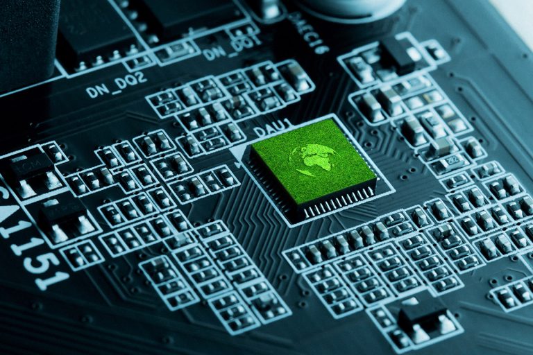 A close-up view of a computer circuit board, featuring a prominent green chip surrounded by intricate circuitry.