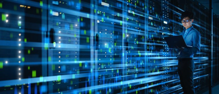 A person in a blue hoodie analyzes data using a laptop in front of glowing server racks, creating a high-tech ambiance.