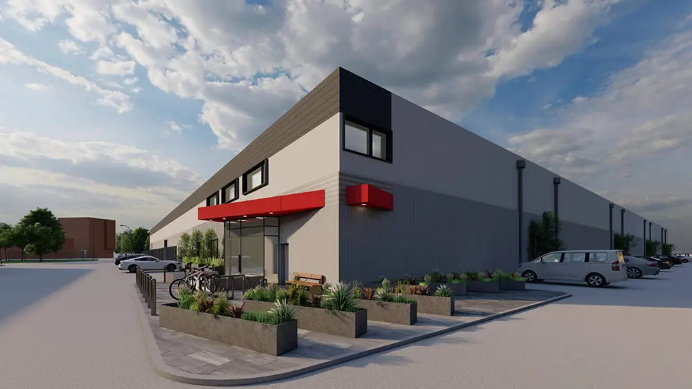 A modern building with a red awning, surrounded by plants and parked cars, under a partly cloudy sky.
