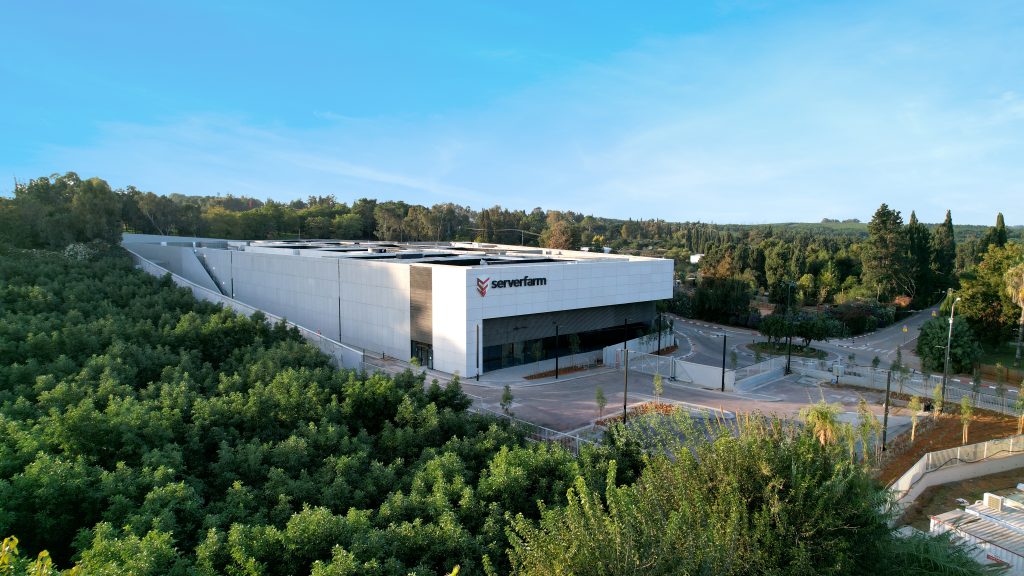 A modern building surrounded by lush greenery and trees, featuring a clear blue sky in the background.