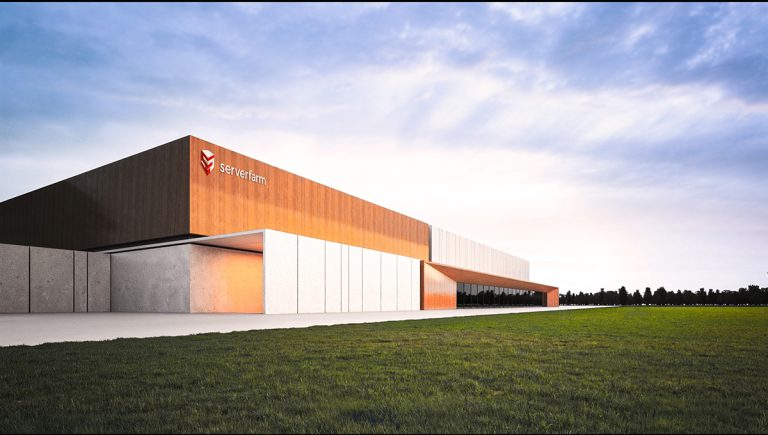 A modern architectural building with a mix of orange and gray exterior, surrounded by grassy land under a clear sky.