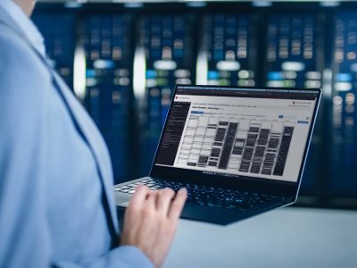 A person in a suit operates a laptop displaying data analysis, with server racks visible in the background.