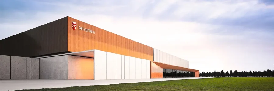 A modern architectural building with a mix of orange and gray exterior, surrounded by grassy land under a clear sky.