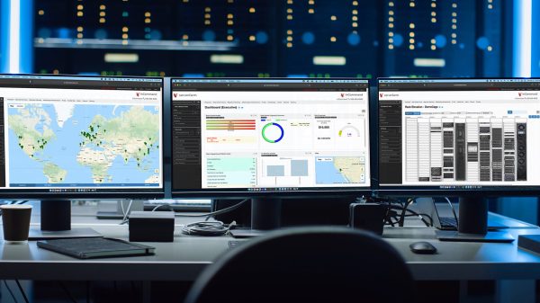 Shot of Multiple Personal Computer Monitors Showing Coding Language Program with System Monitoring Interface. In the Background Data Center with Server Racks.