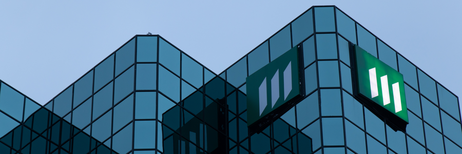 A modern glass building with a green logo prominently displayed on its facade against a twilight sky.