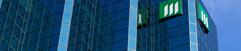 A modern glass building with a distinctive green logo, reflecting the blue sky and showcasing a sleek architectural design.