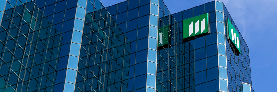 A modern glass building with a distinctive green logo, reflecting the blue sky and showcasing a sleek architectural design.