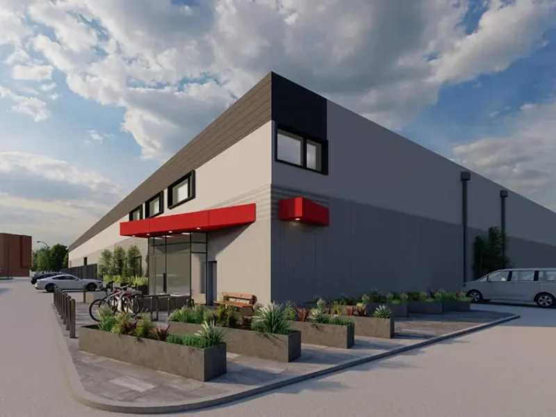 A modern building with a red awning, surrounded by plants and parked cars, under a partly cloudy sky.