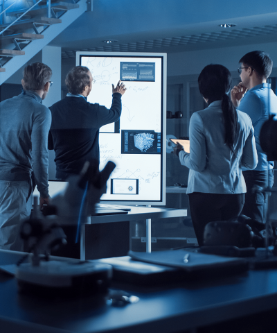 A group of professionals analyzing data on a large screen in a modern lab setting, illuminated by blue light.